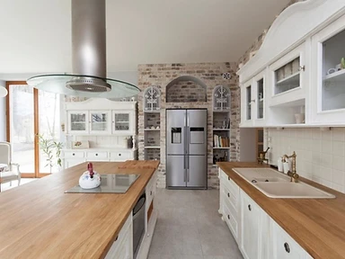 Kitchen with central island, light oak countertops and exposed brick feature wall with stainless steel refrigerator, designed by Tabinets in Lakeville, MA