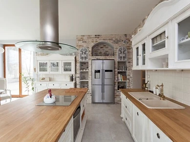Kitchen with central island, light oak countertops and exposed brick feature wall with stainless steel refrigerator, designed by Tabinets in Lakeville, MA
