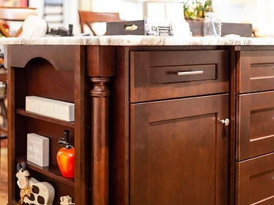 Dark stained wood kitchen island with carved decorative column, open shelving and marble countertop, crafted by Tabinets near Middleborough, MA